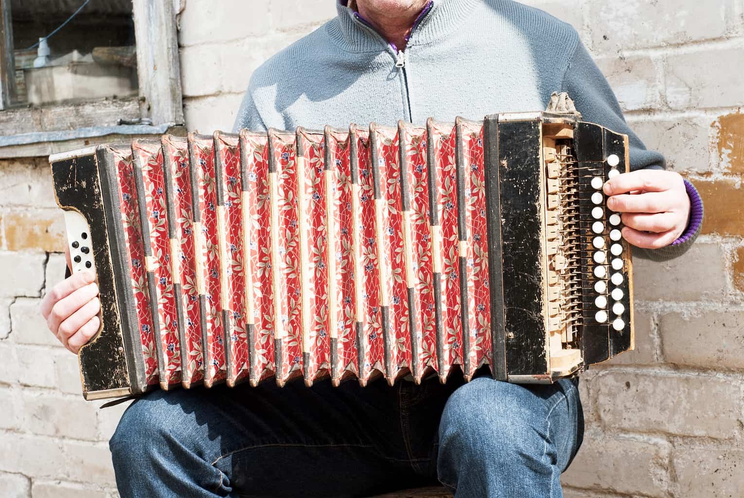 How to Play the Concertina - man playing with an old grunge concertina near the brick wall